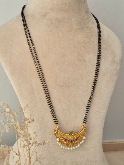 Traditional Indian black beaded mangalsutra chain featuring a gold crescent pendant accented with ruby pink and emerald green stones and pearl droplets