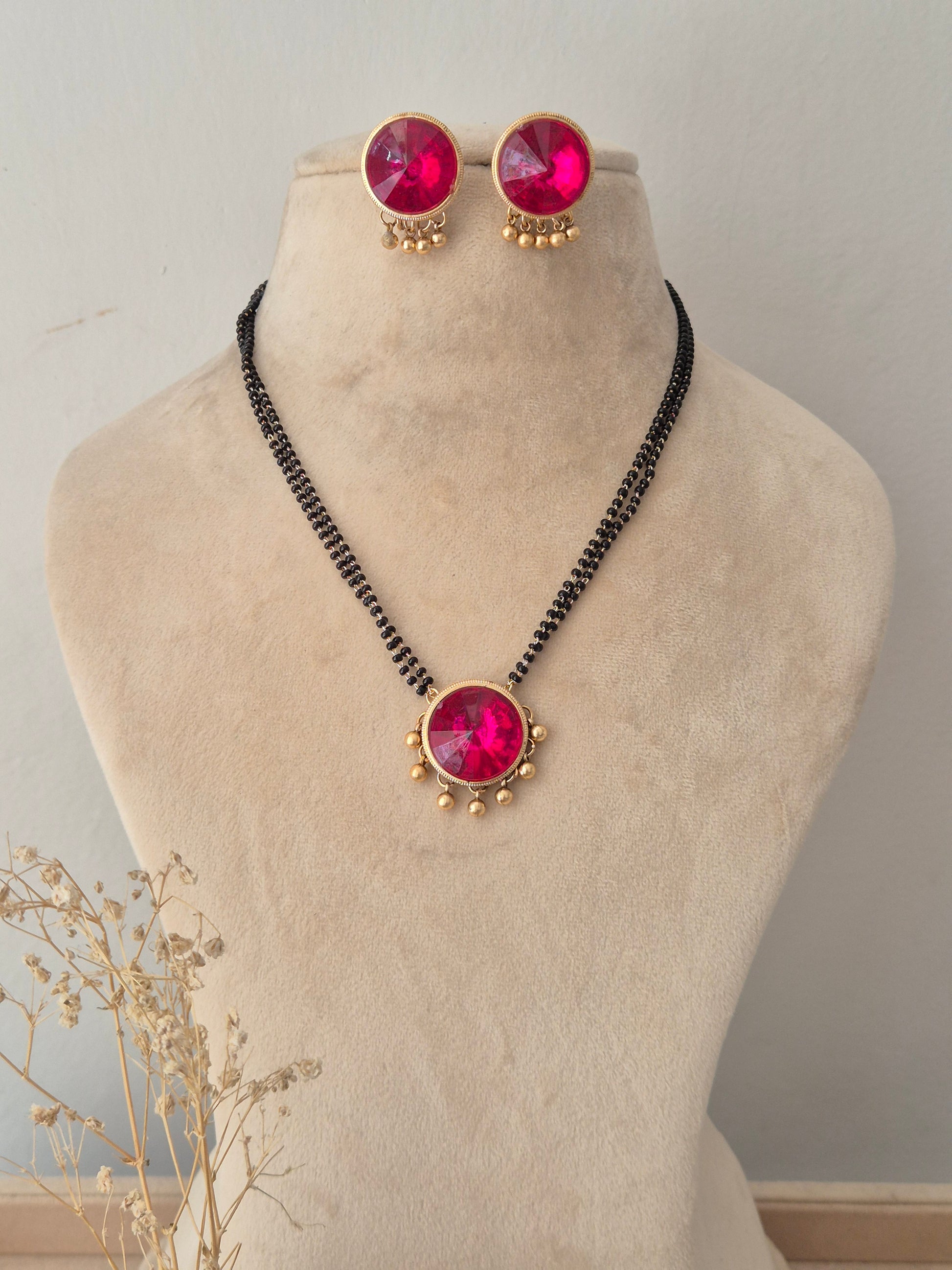 Pranati Mangalsutra Set – Multi-strand black beaded chain with a large round magenta stone pendant and matching round pink stud earrings