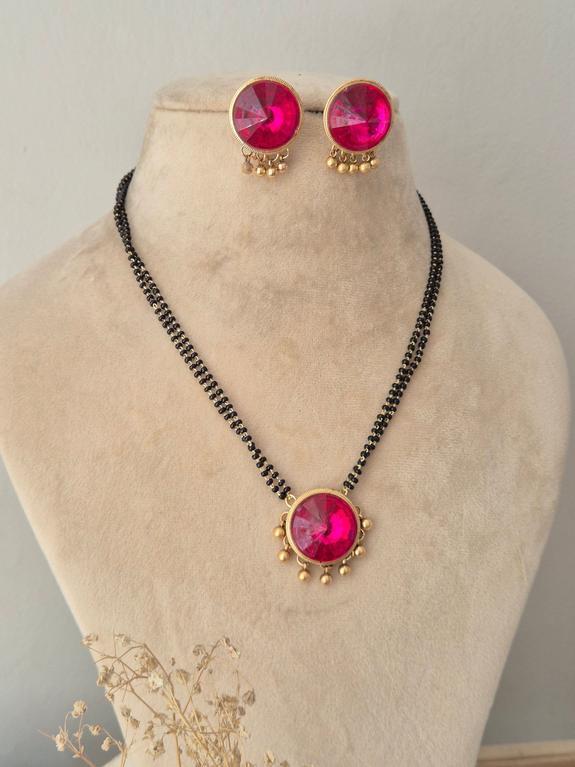 Traditional black beaded mangalsutra necklace paired with round pink gemstone stud earrings accented with hanging gold beads