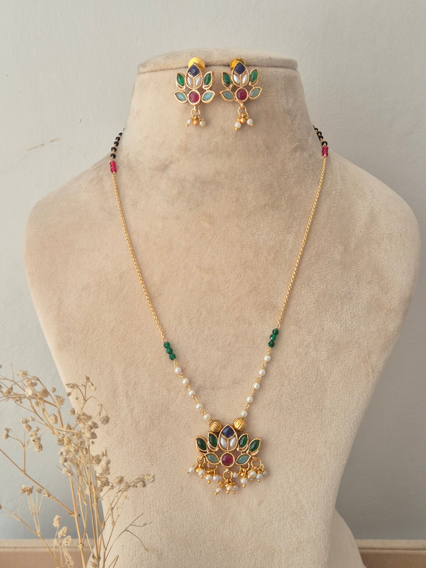 Luvina Necklace Set featuring a thin gold chain with green, pink, and white bead accents, a floral lotus-shaped kundan pendant, and matching floral stud earrings