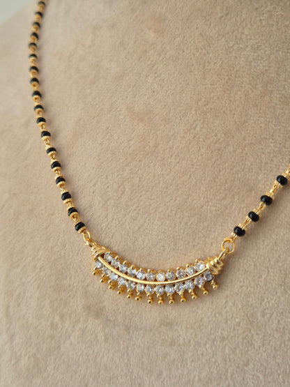Gold and black beaded necklace with a curved pendant set with clear stones, displayed on a beige textured jewelry bust.
