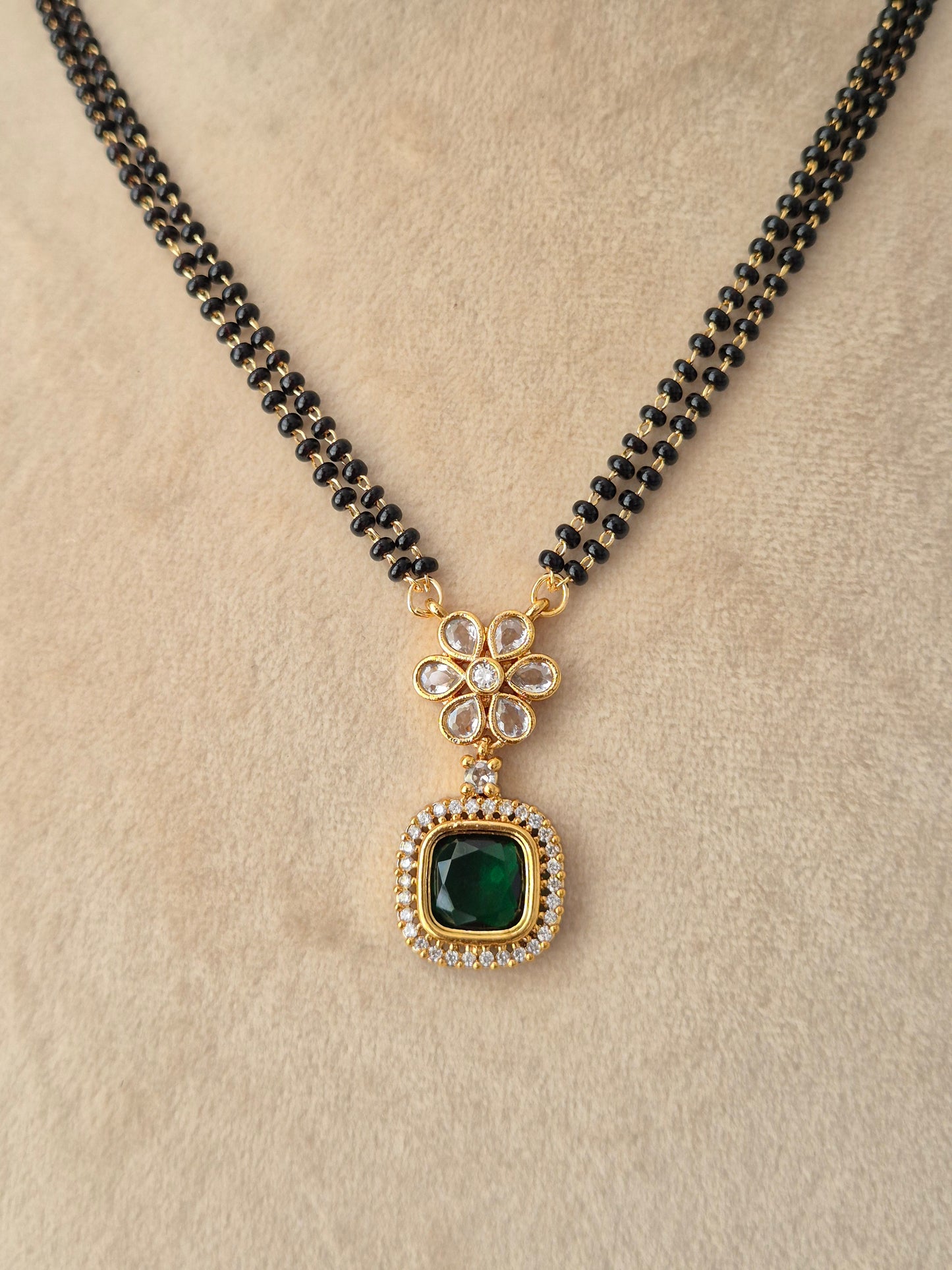A black beaded necklace with a gold-toned pendant featuring a green square stone