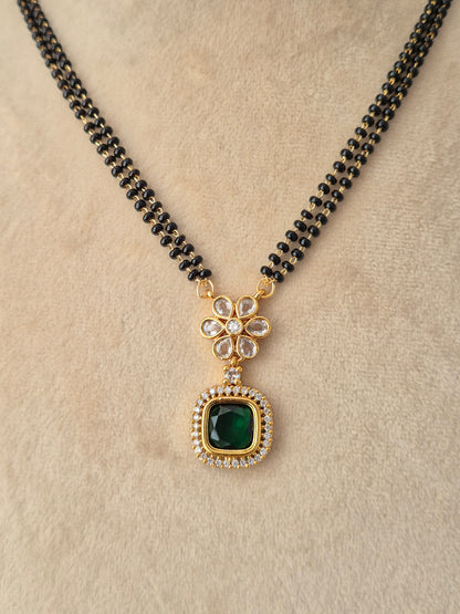 A black beaded necklace with a gold-toned pendant featuring a green square stone