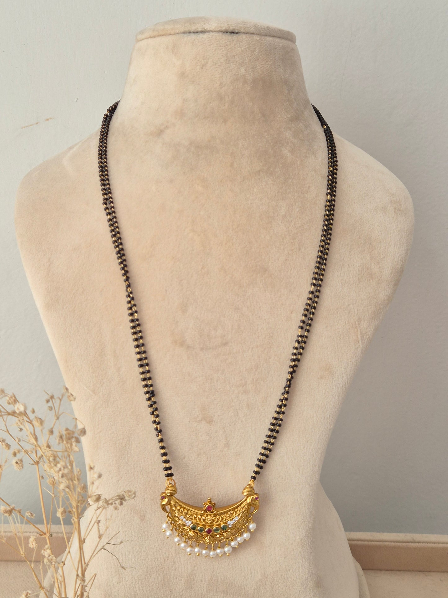 Traditional black-beaded Padmini Mangalsutra featuring a gold crescent pendant embellished with red and green stones and tiny pearl drops