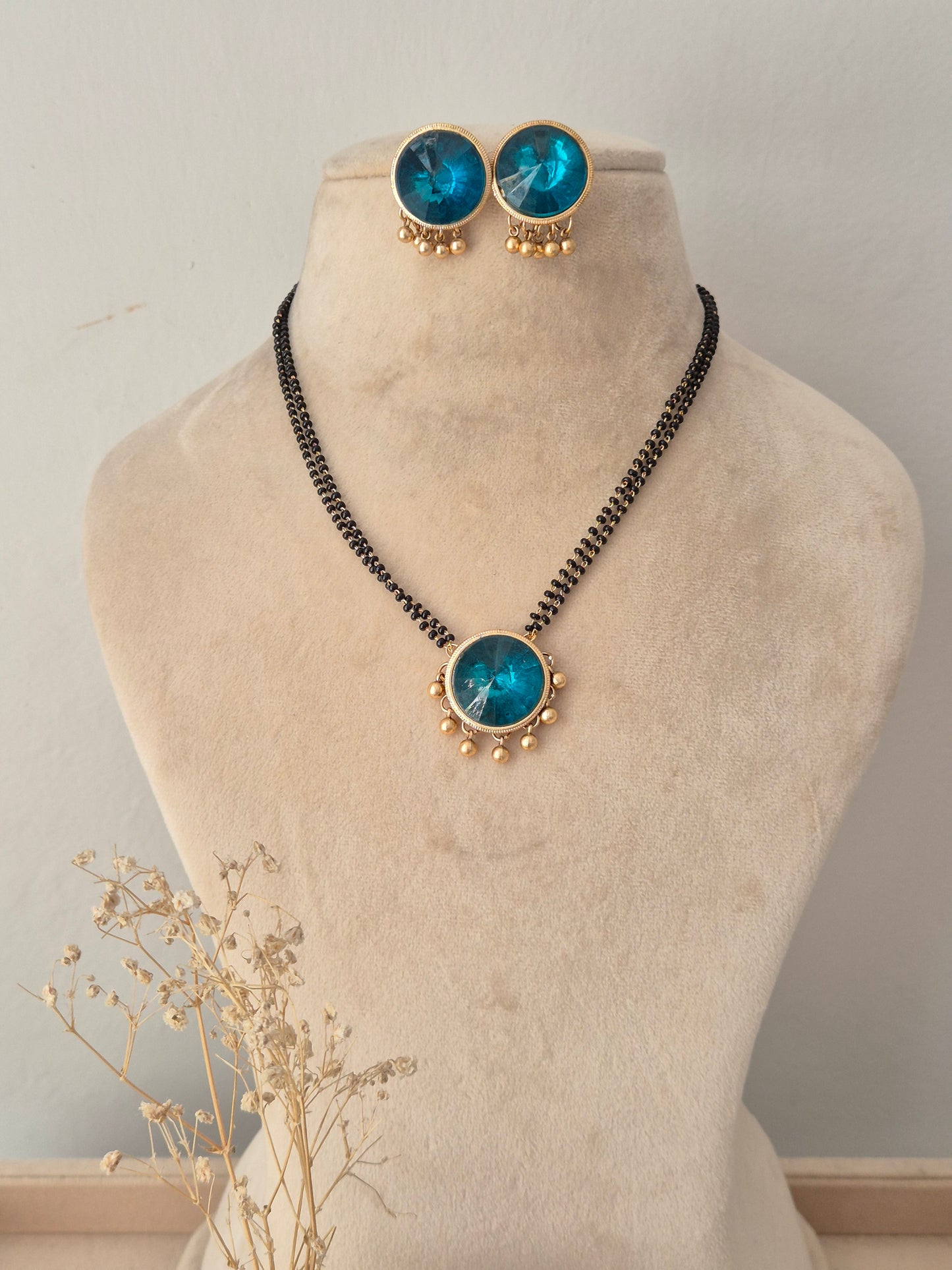 Preyasi Mangalsutra set featuring a double-strand black bead chain connected to a round gold-framed turquoise blue stone pendant with gold bead accents, paired with matching circular stud earrings