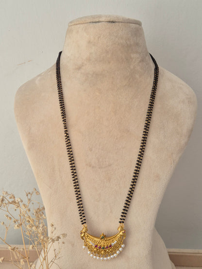 Traditional long black-beaded Janani Mangalsutra featuring a gold crescent pendant with colorful stones and white pearl drops