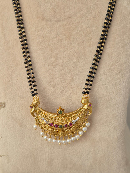 Close-up view of the Janani Mangalsutra crescent gold pendant with red and green stones, pearl drops, and black-beaded chain