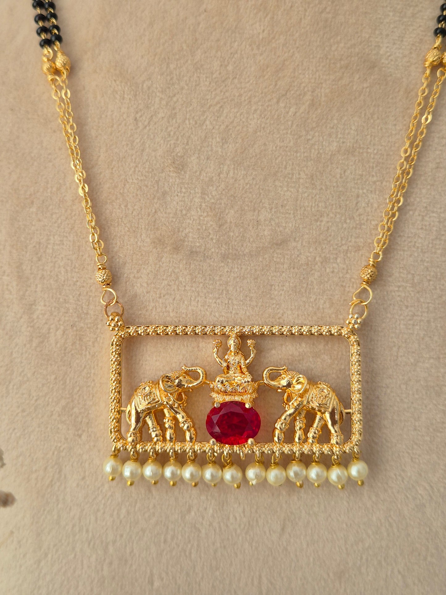 Close-up of gold Jivinta Mangalsutra pendant with twin elephant motifs, central red oval stone, and white pearl drops
