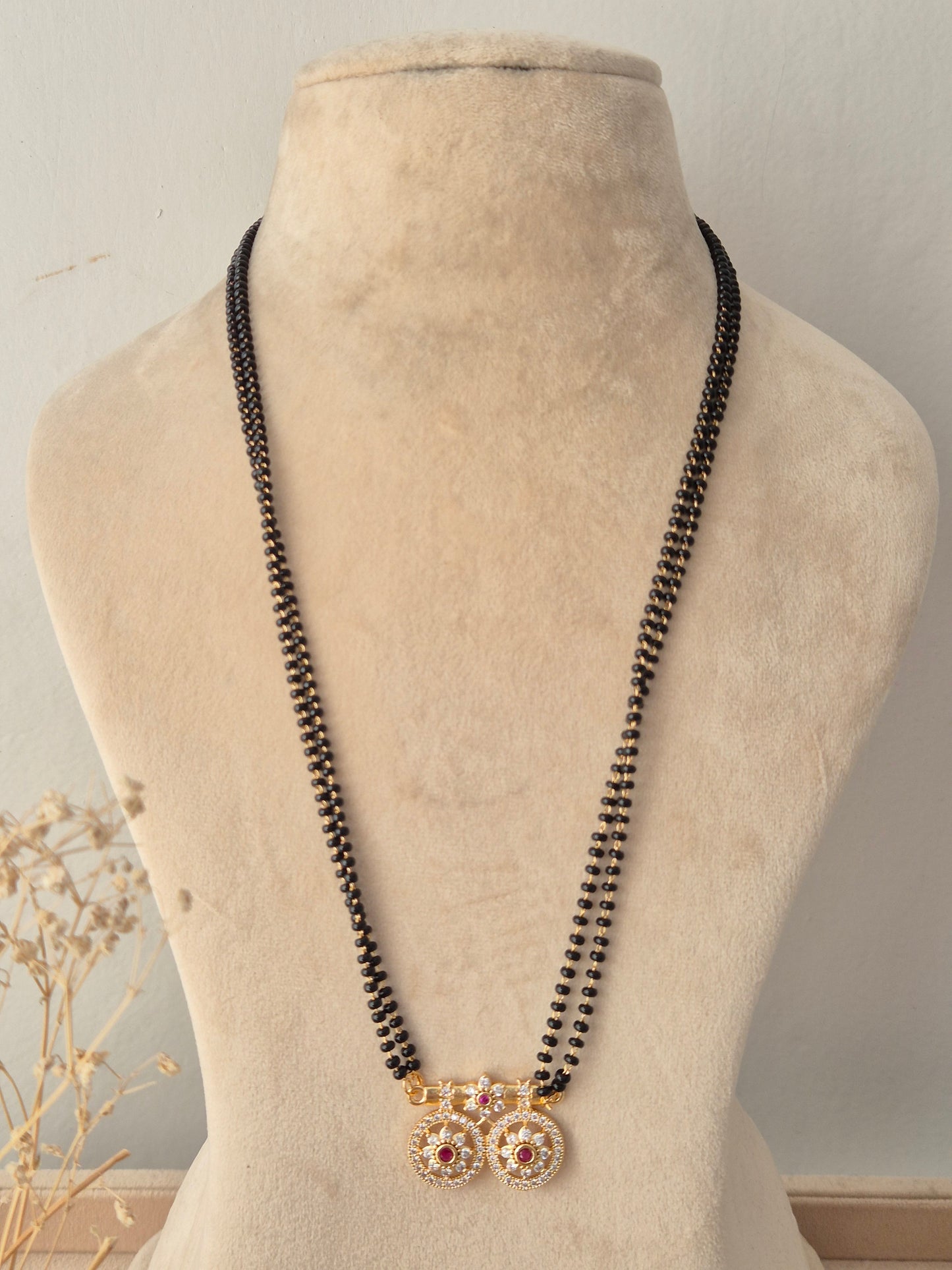 Traditional long Baani Mangalsutra featuring twin circular gold floral pendants studded with red and clear CZ stones on a black-beaded chain