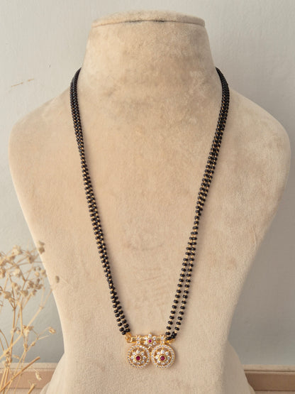 Traditional long Baani Mangalsutra featuring twin circular gold floral pendants studded with red and clear CZ stones on a black-beaded chain