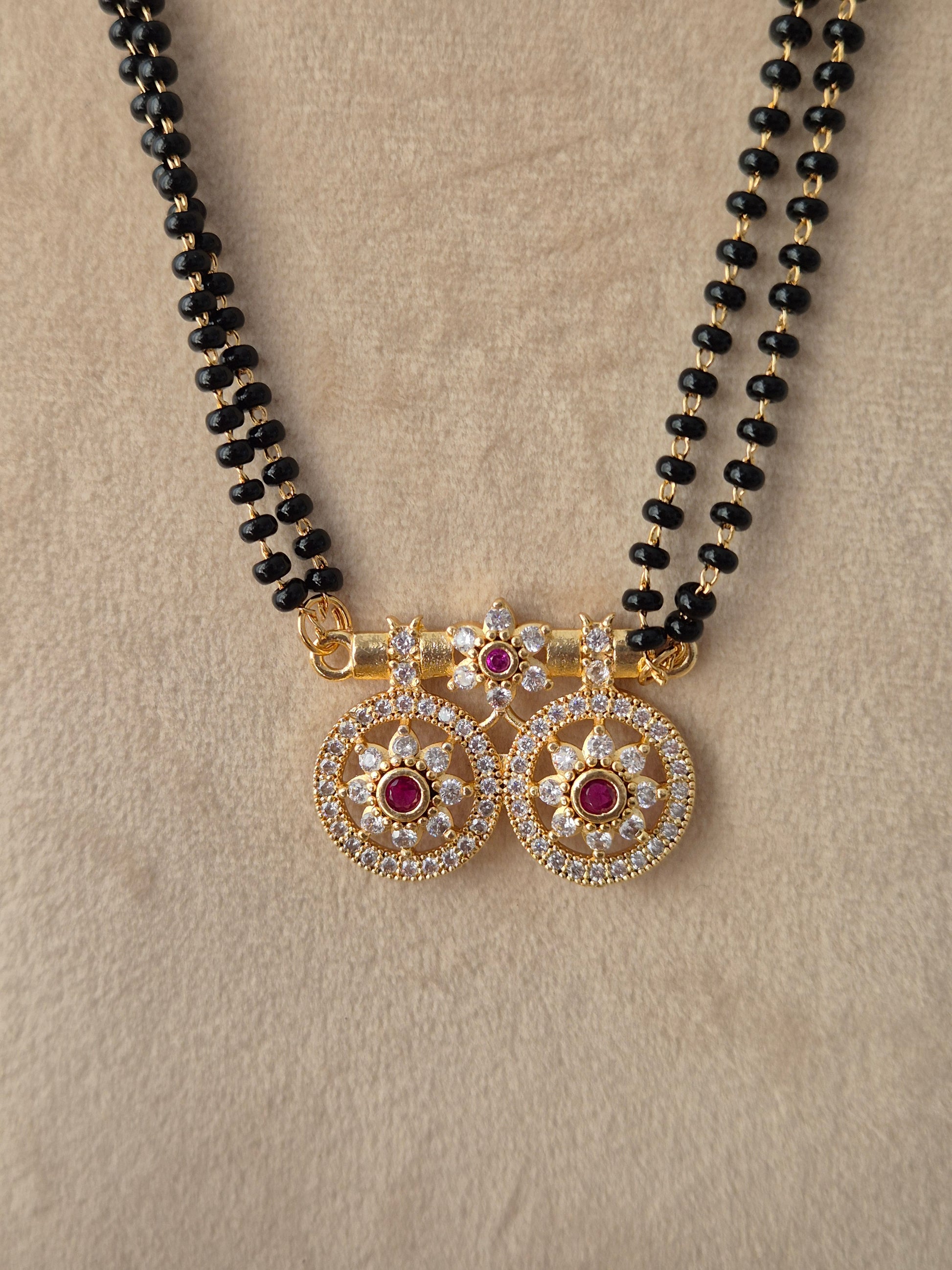 Baani Mangalsutra gold win floral pendant close-up with red and clear CZ stones and black beads chain by Naitri