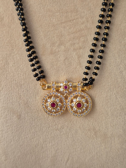 Baani Mangalsutra gold win floral pendant close-up with red and clear CZ stones and black beads chain by Naitri