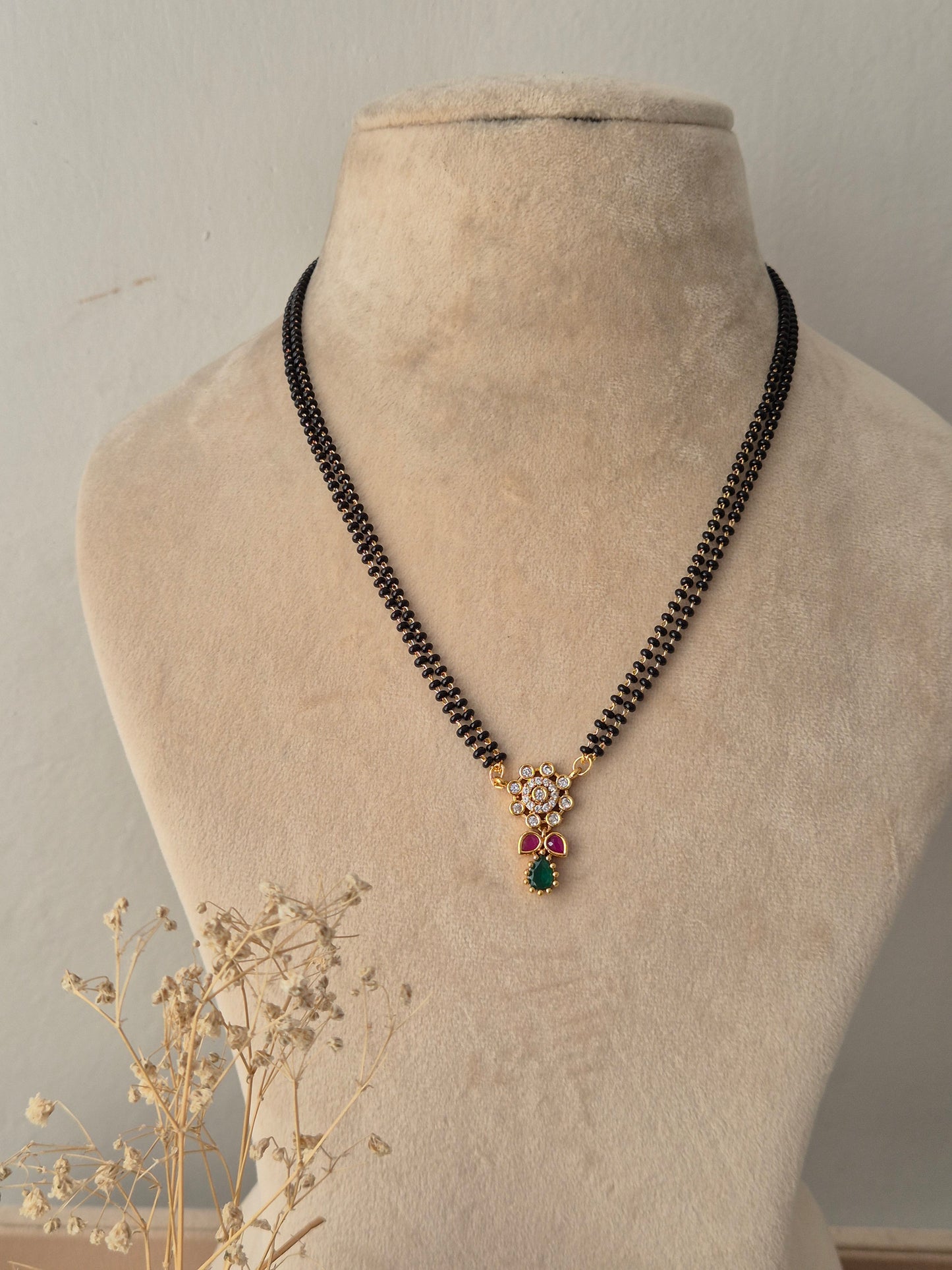Traditional gold Anjika Mangalsutra with a floral CZ pendant, green teardrop drop, and black-beaded chain
