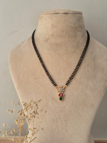 Traditional gold Anjika Mangalsutra with a floral CZ pendant, green teardrop drop, and black-beaded chain