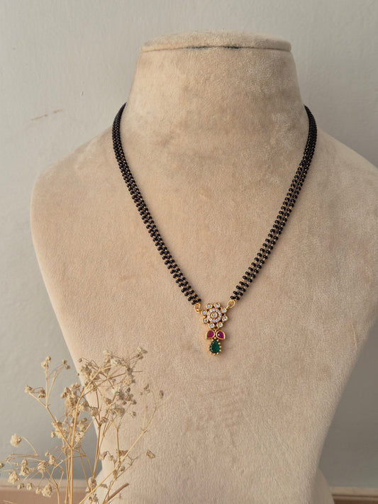 Traditional gold Anjika Mangalsutra with a floral CZ pendant, green teardrop drop, and black-beaded chain