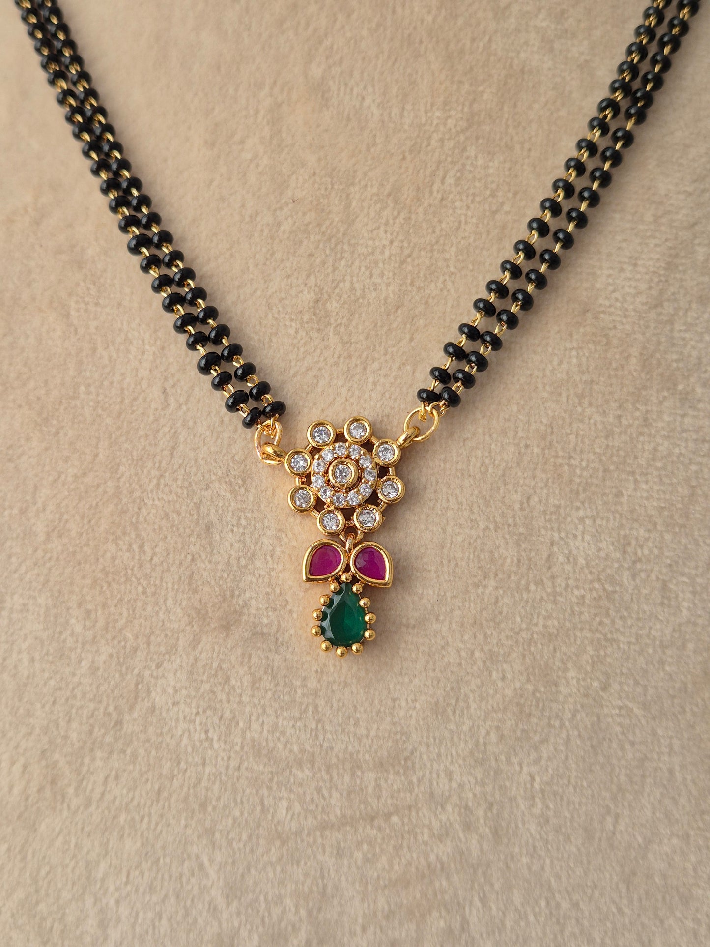 njika Mangalsutra gold floral pendant close-up with CZ stones, pink accents, green teardrop drop, and black beads necklace by Naitri