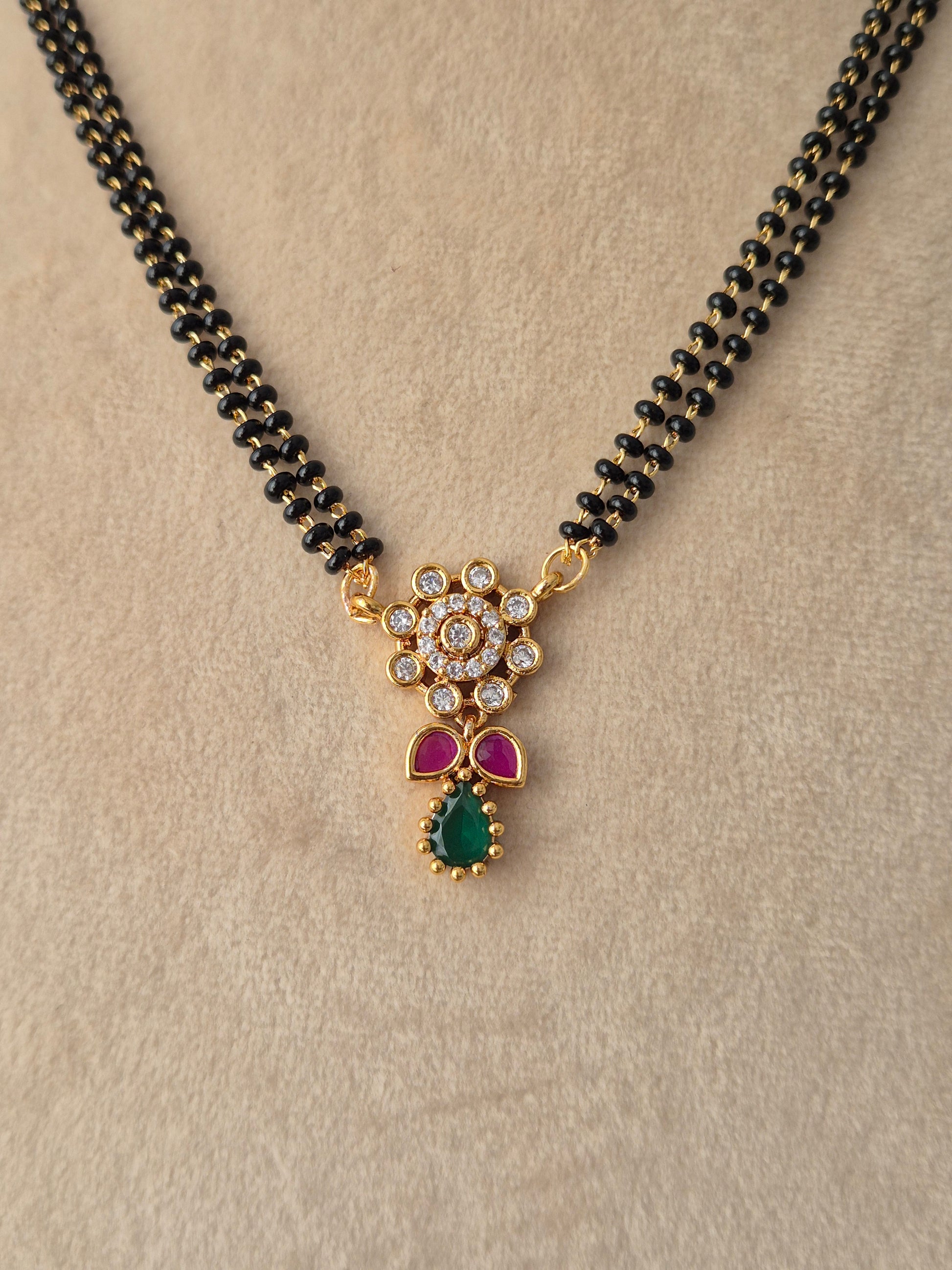 njika Mangalsutra gold floral pendant close-up with CZ stones, pink accents, green teardrop drop, and black beads necklace by Naitri
