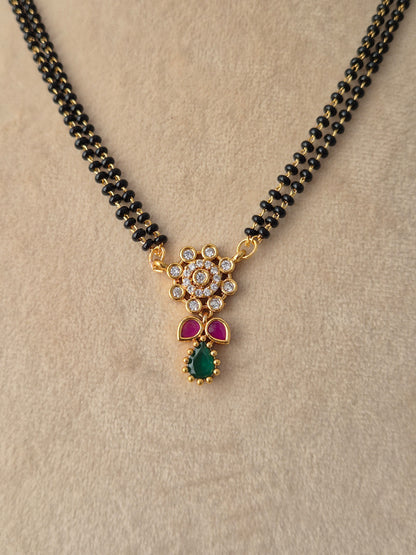 njika Mangalsutra gold floral pendant close-up with CZ stones, pink accents, green teardrop drop, and black beads necklace by Naitri