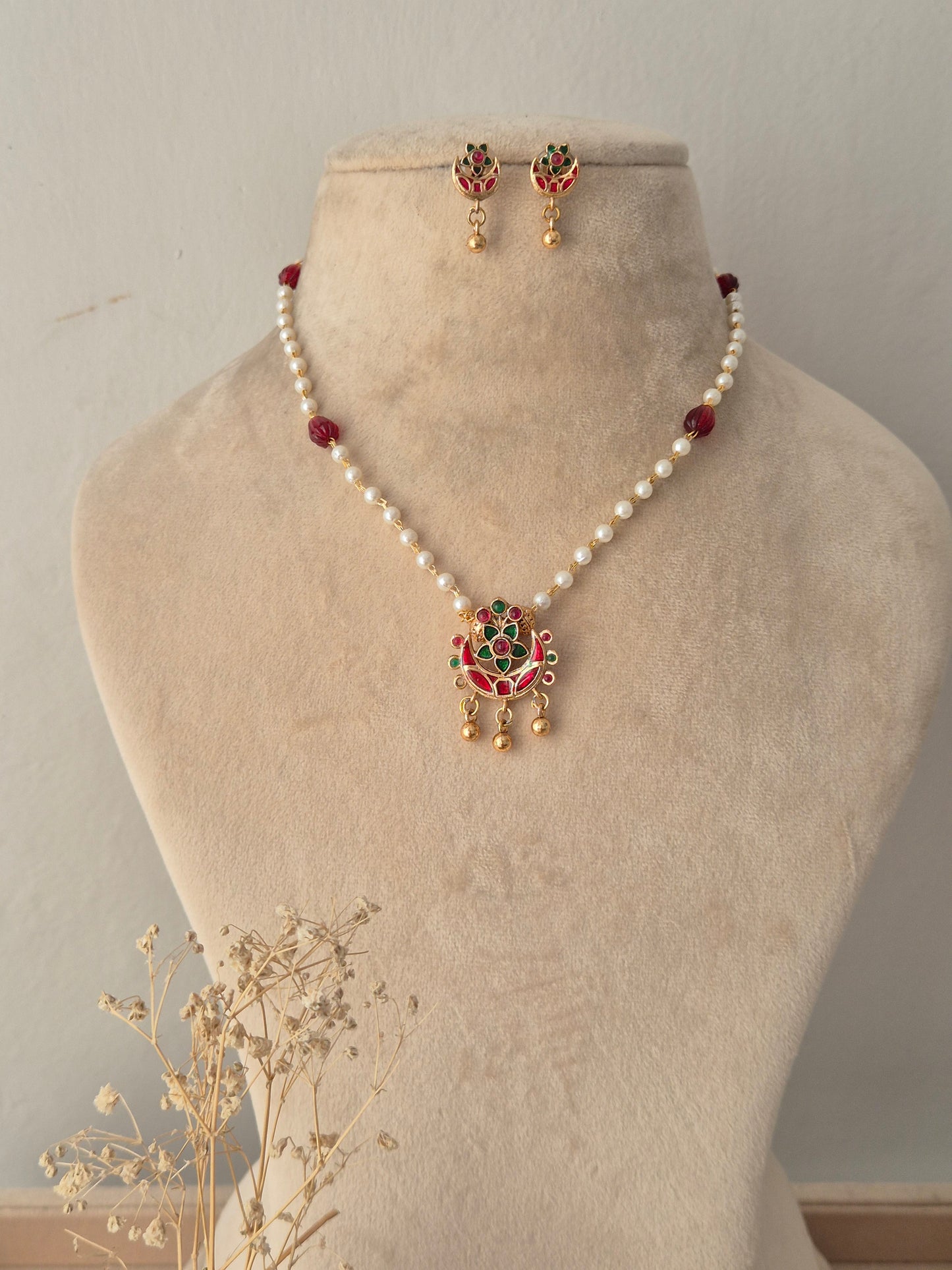 Aloka Necklace Set featuring a white pearl beaded chain with a red and green stone gold pendant and matching drop earrings