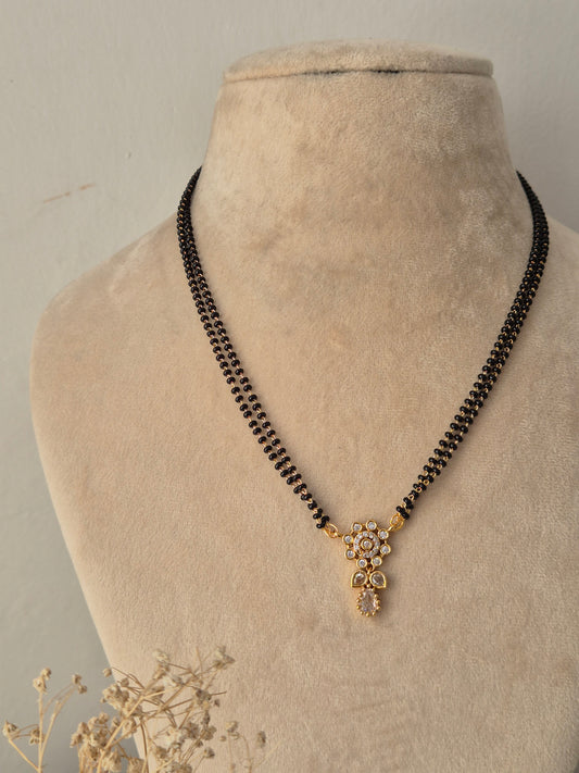 Chetasi Mangalsutra featuring a double-strand black bead chain connected to a small gold floral pendant studded with clear CZ stones and a teardrop drop