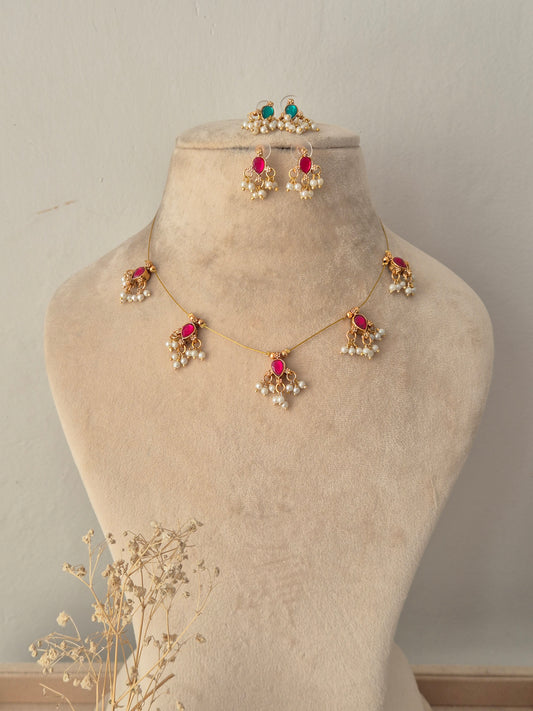 Reversible Ari invisible chain necklace with pink tear-drop stone motifs and dangling pearl beads, displayed on a beige jewelry bust with matching earrings