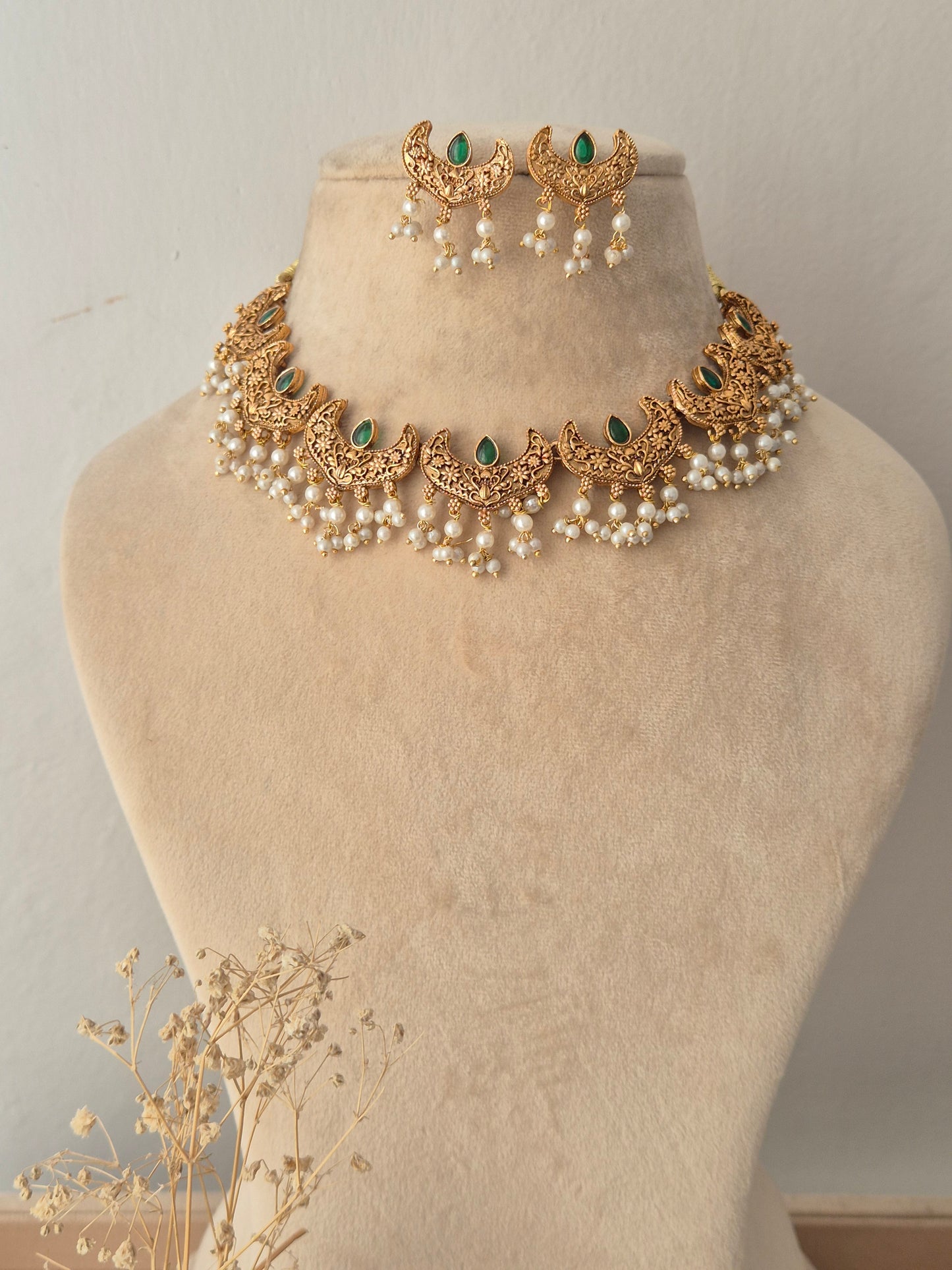 Urjani Necklace Set featuring a gold choker with green stones and pearl drops, displayed with matching crescent earrings
