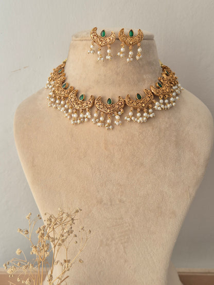 Urjani Necklace Set featuring a gold choker with green stones and pearl drops, displayed with matching crescent earrings