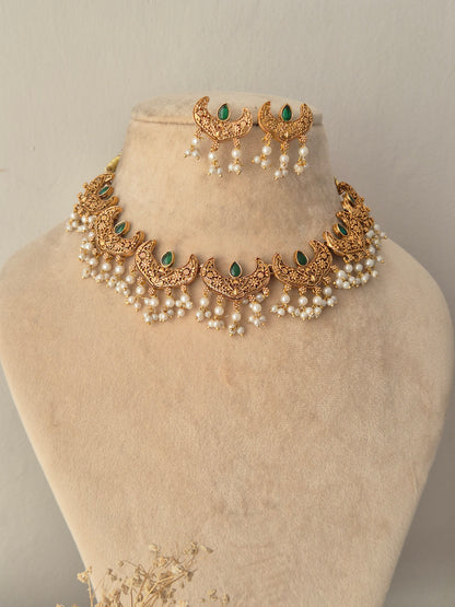 Urjani Necklace Set showcasing a gold-toned choker necklace with crescent-shaped motifs, green gemstone accents, and hanging white pearl clusters, paired with matching crescent drop earrings