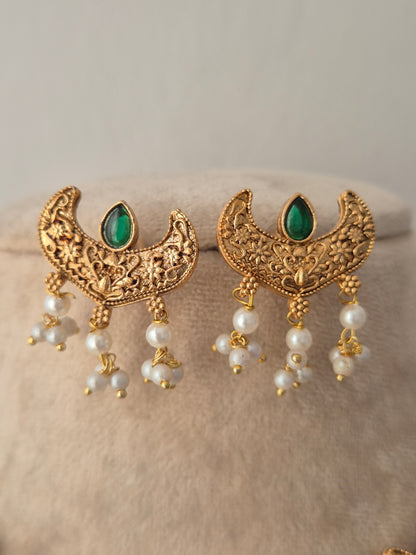 Pair of gold crescent-shaped earrings with green stones and dangling white pearls from the Urjani Necklace Set