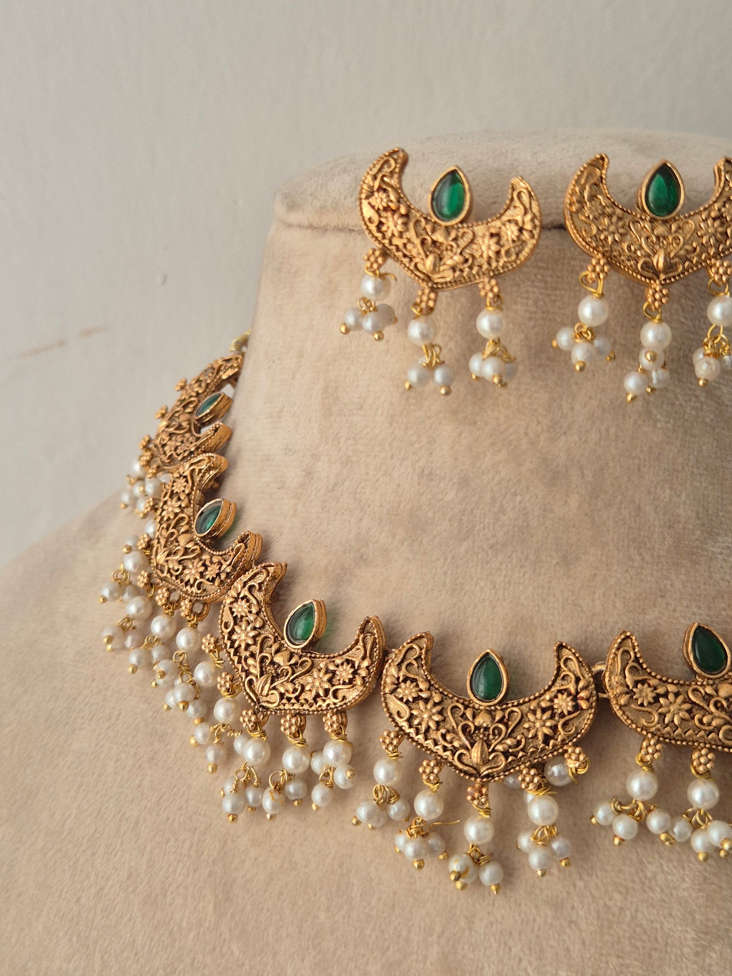 Close-up of the Urjani gold choker necklace and matching crescent earrings with green stones and pearl drops
