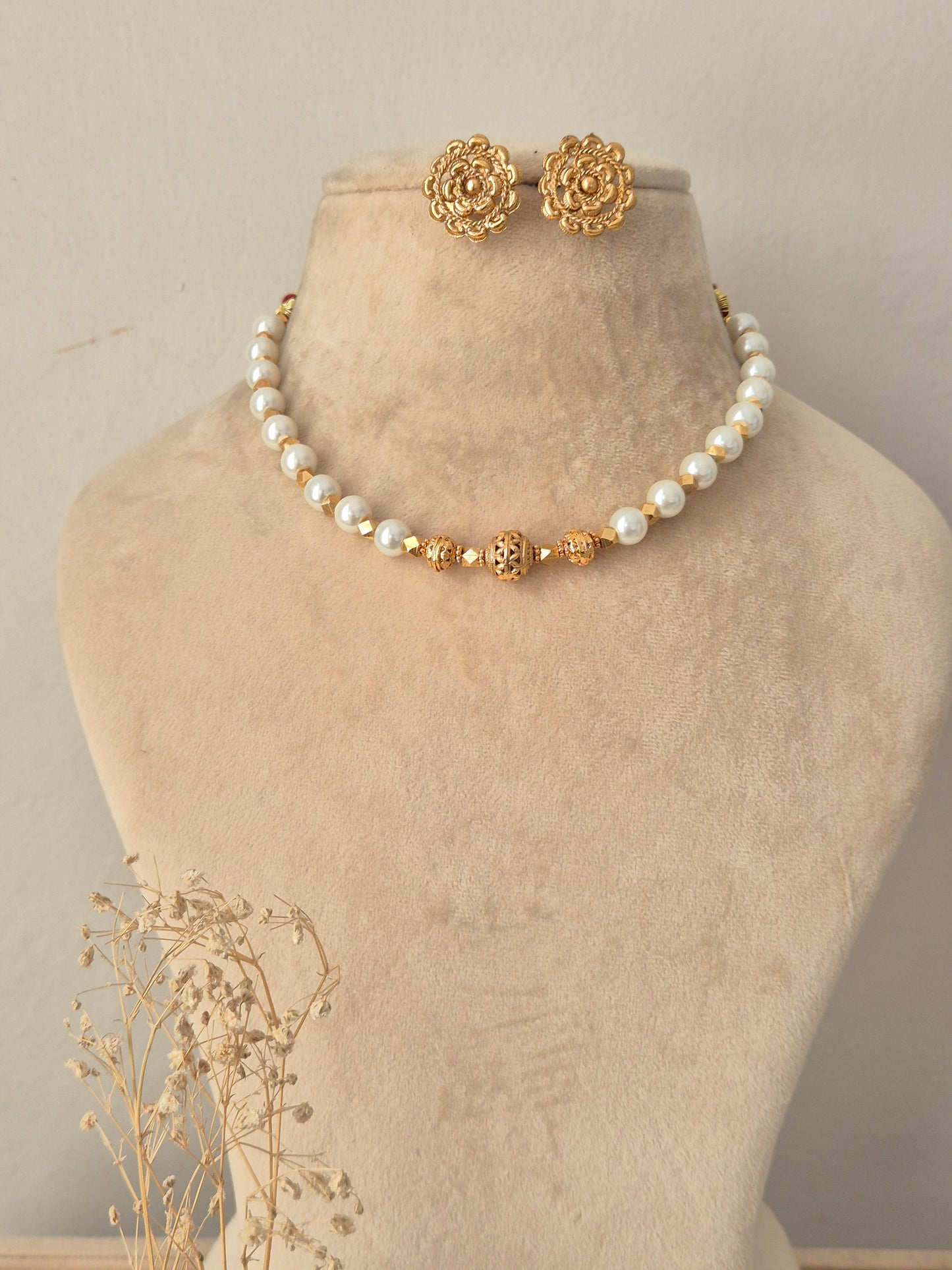 Bhoomija Necklace Set featuring a white pearl strand with carved gold central beads and matching floral gold stud earrings