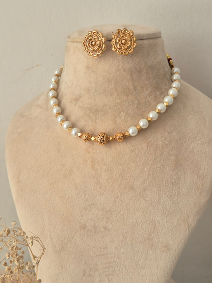 Bhoomija Necklace Set featuring a single strand of white pearls accented with intricate gold spacer beads and a carved central bead, paired with matching layered floral gold stud earrings