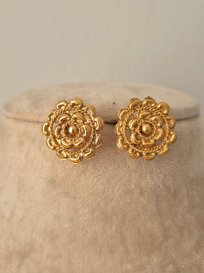 Close-up of a pair of gold-toned circular stud earrings featuring an intricate multi-layered floral design with textured rope-style borders