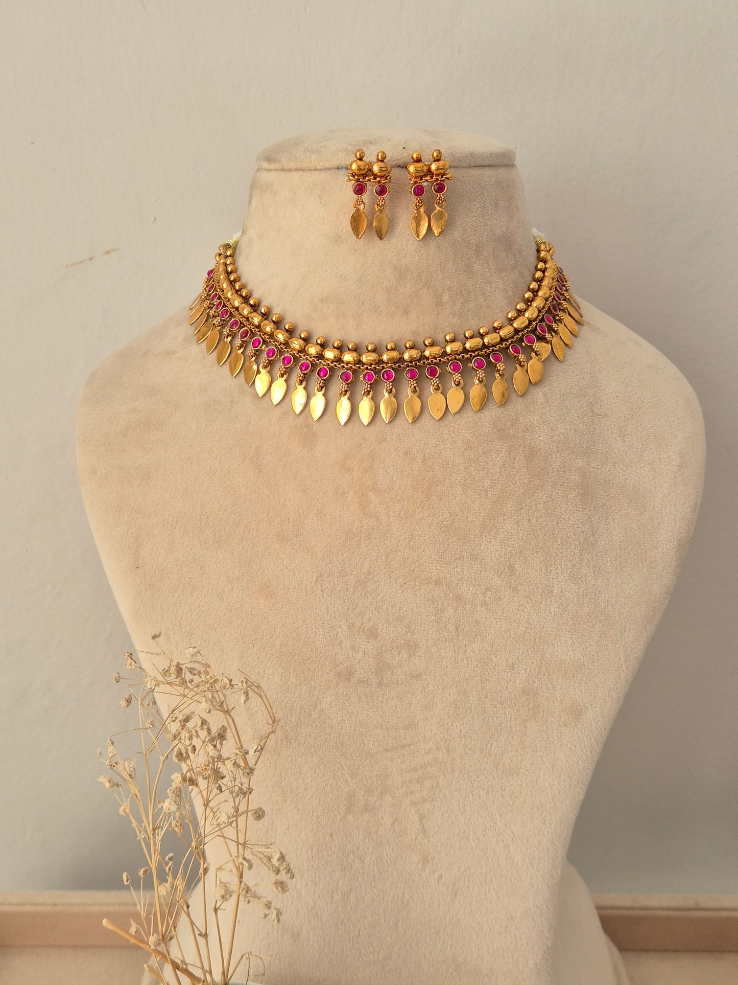 Pahal Necklace Set featuring a gold choker with pink stone accents and dangling leaf charms, paired with matching drop earrings
