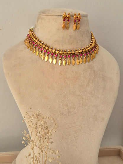 Pahal Necklace Set showcasing an antique gold-toned choker embellished with round pink stones, gold bead accents, and hanging leaf-shaped charms, displayed on a beige mannequin bust alongside matching drop earrings