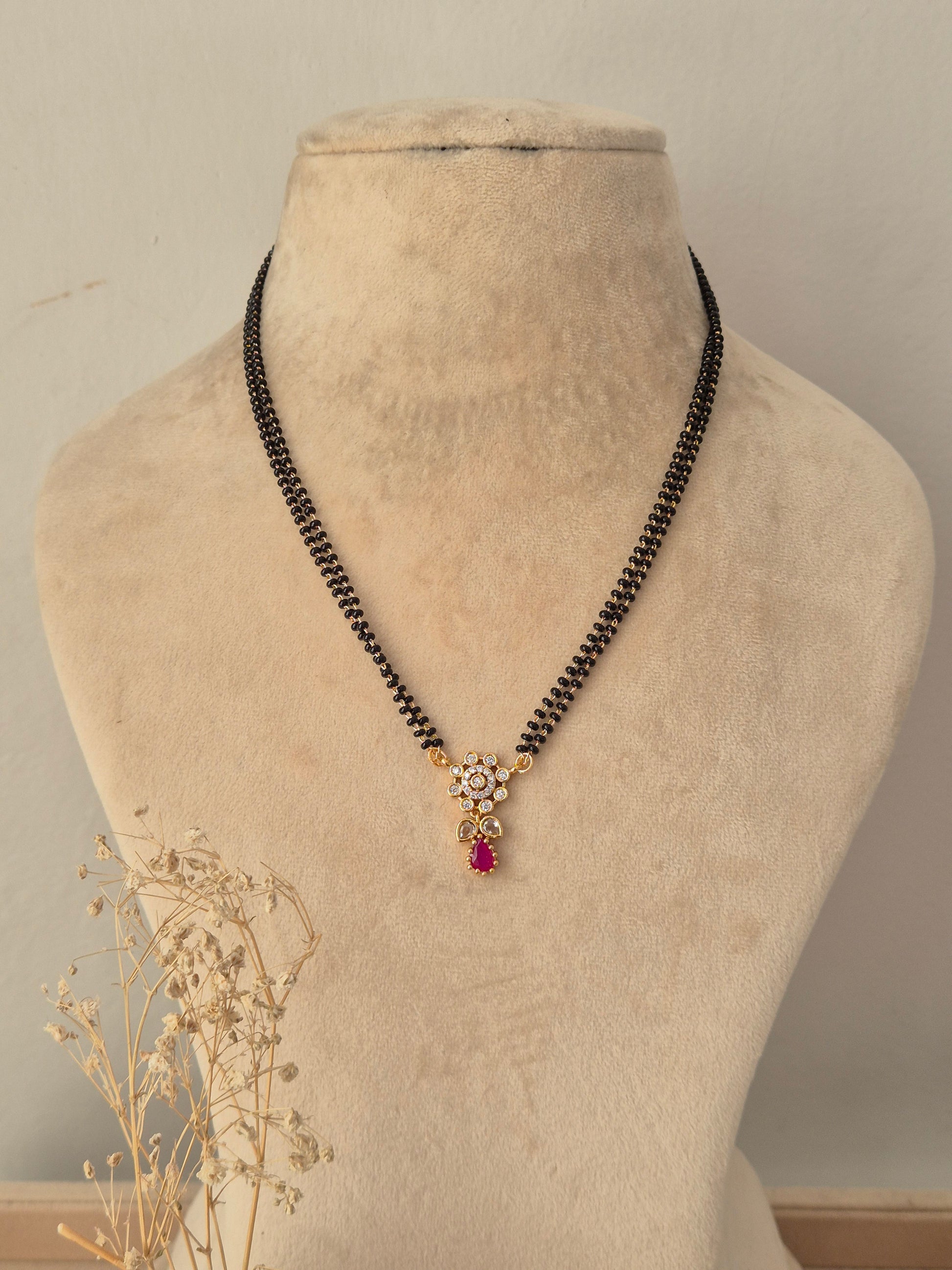 
Sitika Mangalsutra featuring a double-strand black beaded chain and a gold floral CZ pendant with a pink teardrop stone drop