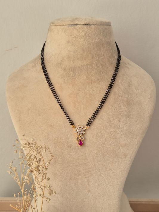 
Sitika Mangalsutra featuring a double-strand black beaded chain and a gold floral CZ pendant with a pink teardrop stone drop
