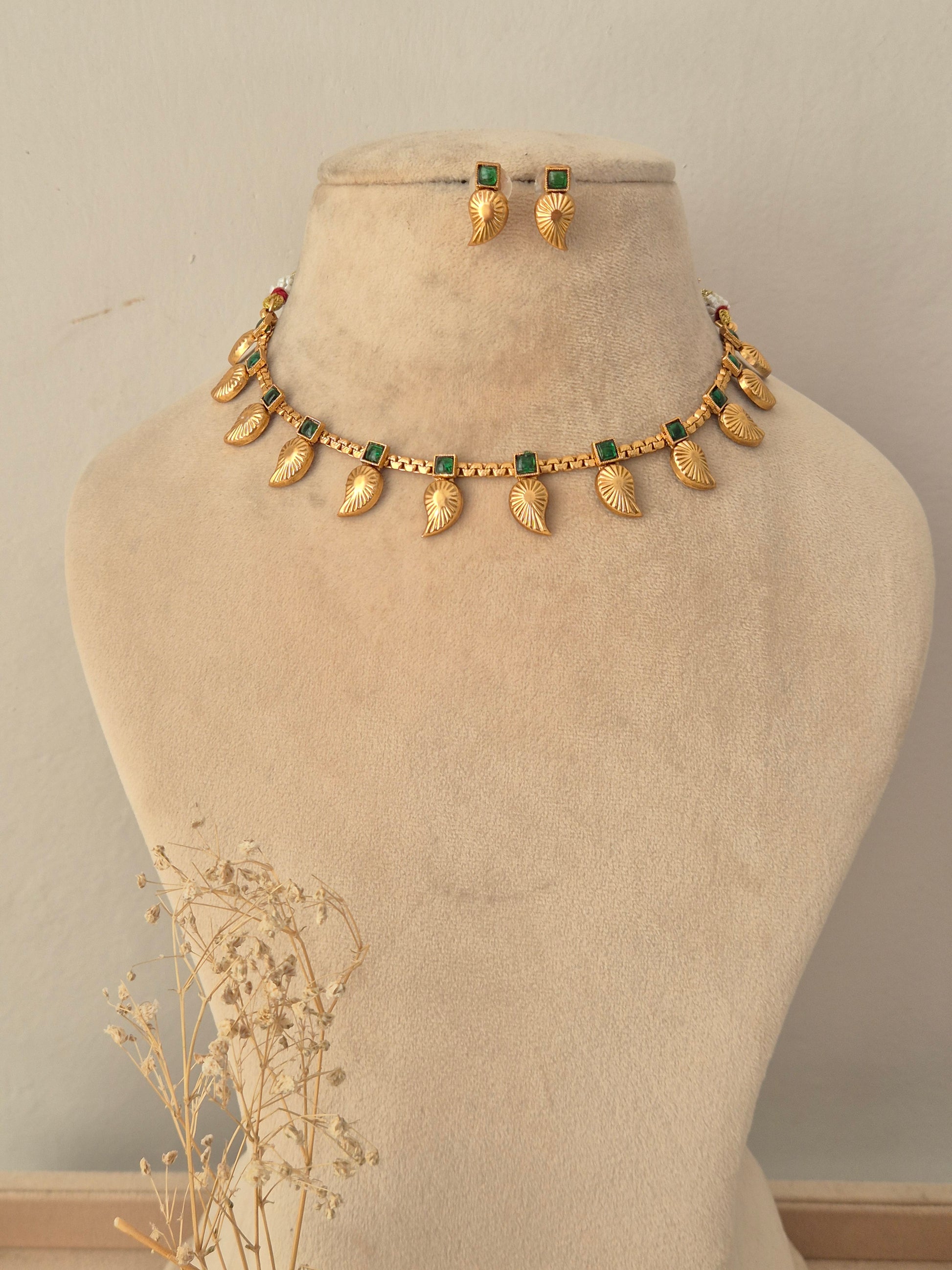 Tanvika Necklace Set featuring a gold choker with green stone accents and dangling leaf charms, paired with matching drop earrings