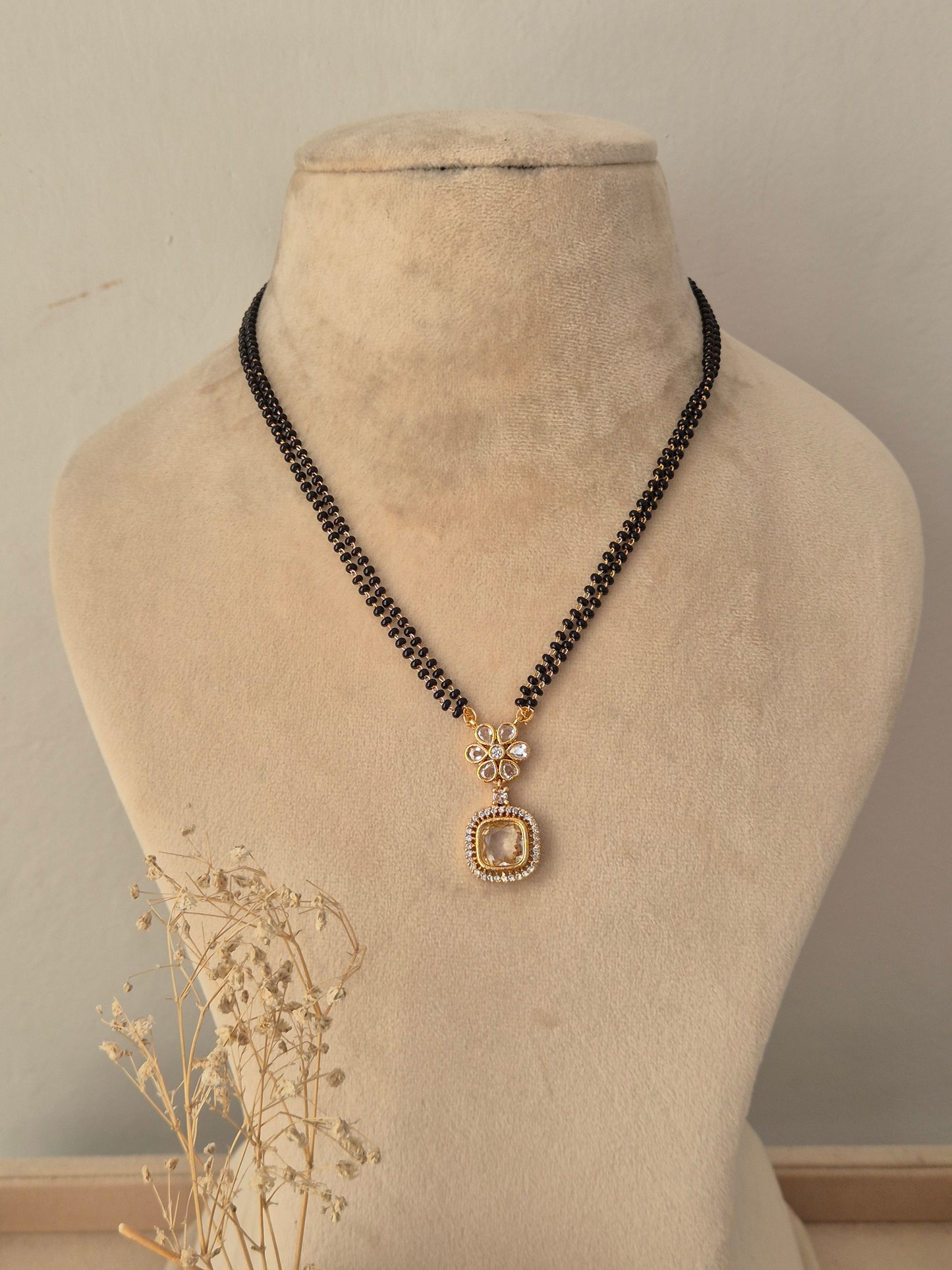 Kavika Mangalsutra featuring a double-strand black beaded chain with a gold floral CZ pendant and teardrop drop