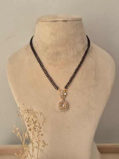 Kavika Mangalsutra featuring a double-strand black beaded chain with a gold floral CZ pendant and teardrop drop