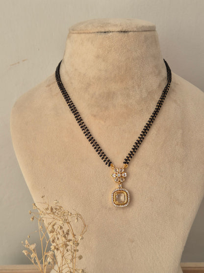 Kavika Mangalsutra featuring a traditional double-strand black and gold bead chain paired with a central gold-toned floral pendant studded with clear CZ stones and finished with a hanging teardrop accent
