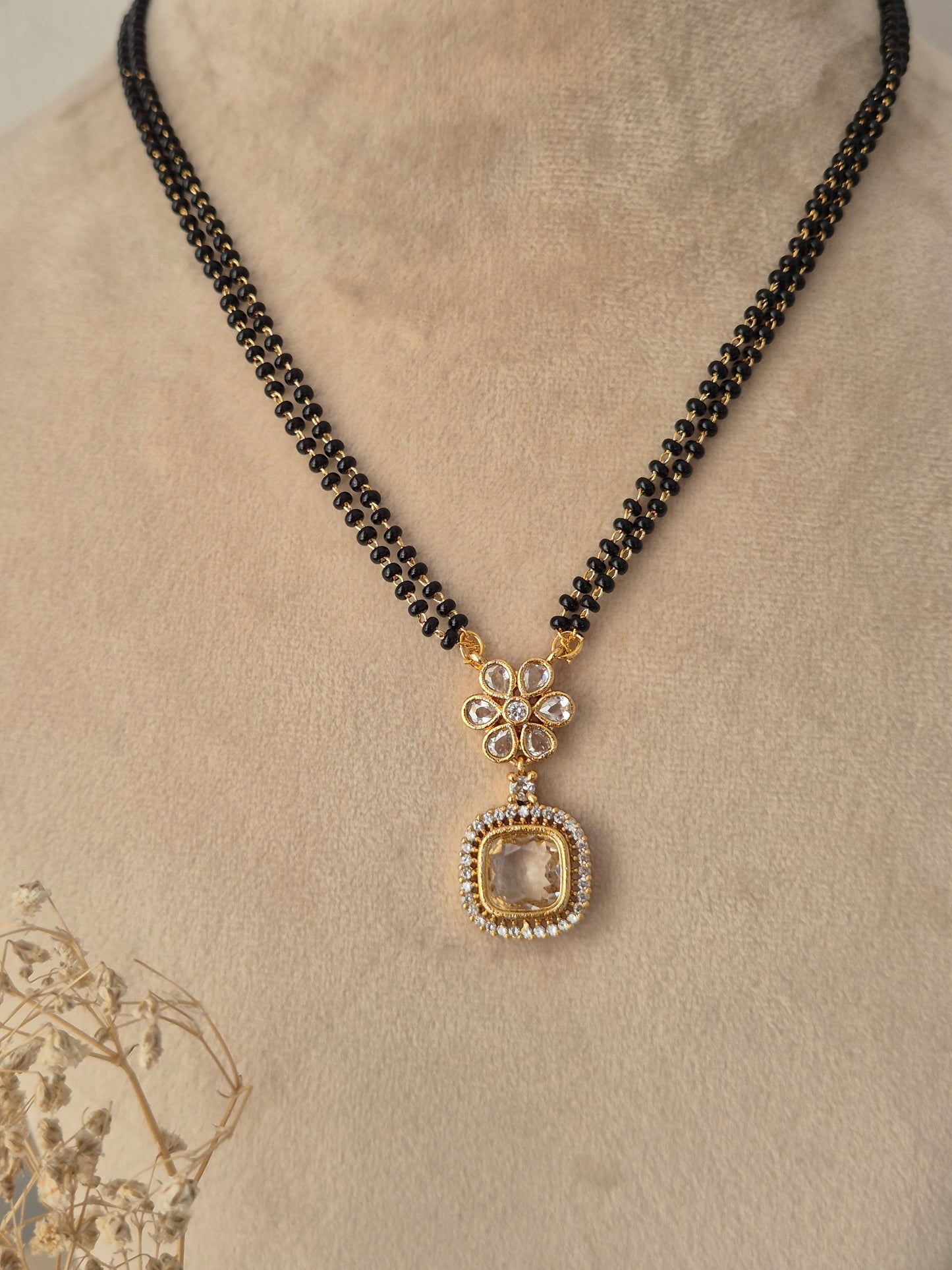 Close-up view of the Kavika Mangalsutra gold floral CZ pendant with a dangling teardrop accent and black bead chain