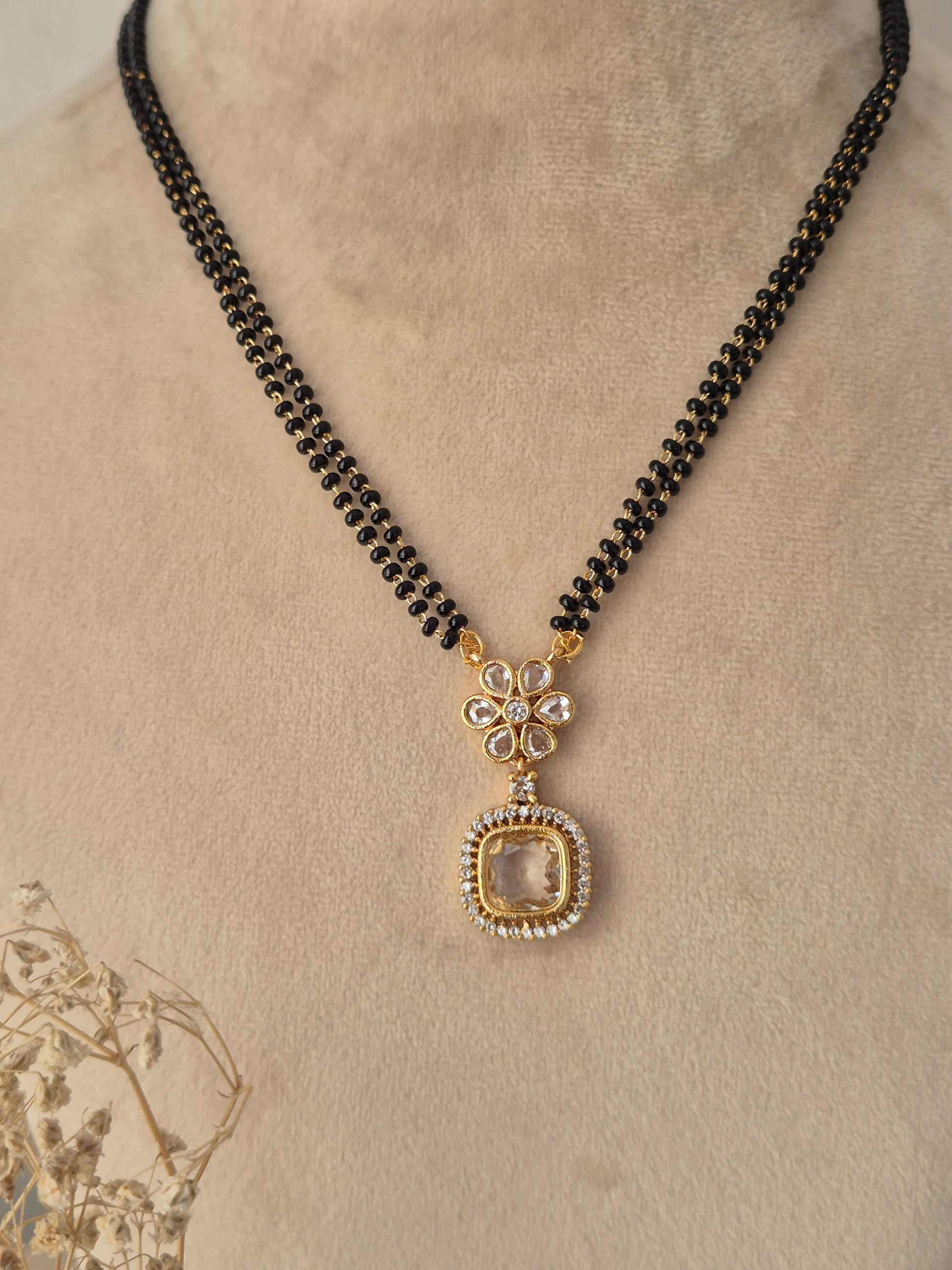 Close-up view of the Kavika Mangalsutra gold floral CZ pendant with a dangling teardrop accent and black bead chain