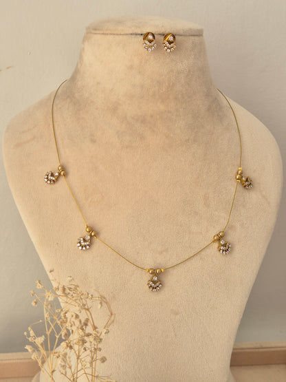 Ishrat Invisible Necklace Chain Set featuring a fine gold wire chain adorned with five evenly spaced floral CZ stone charms, displayed on a beige mannequin bust with matching CZ stud earrings and dried floral accents