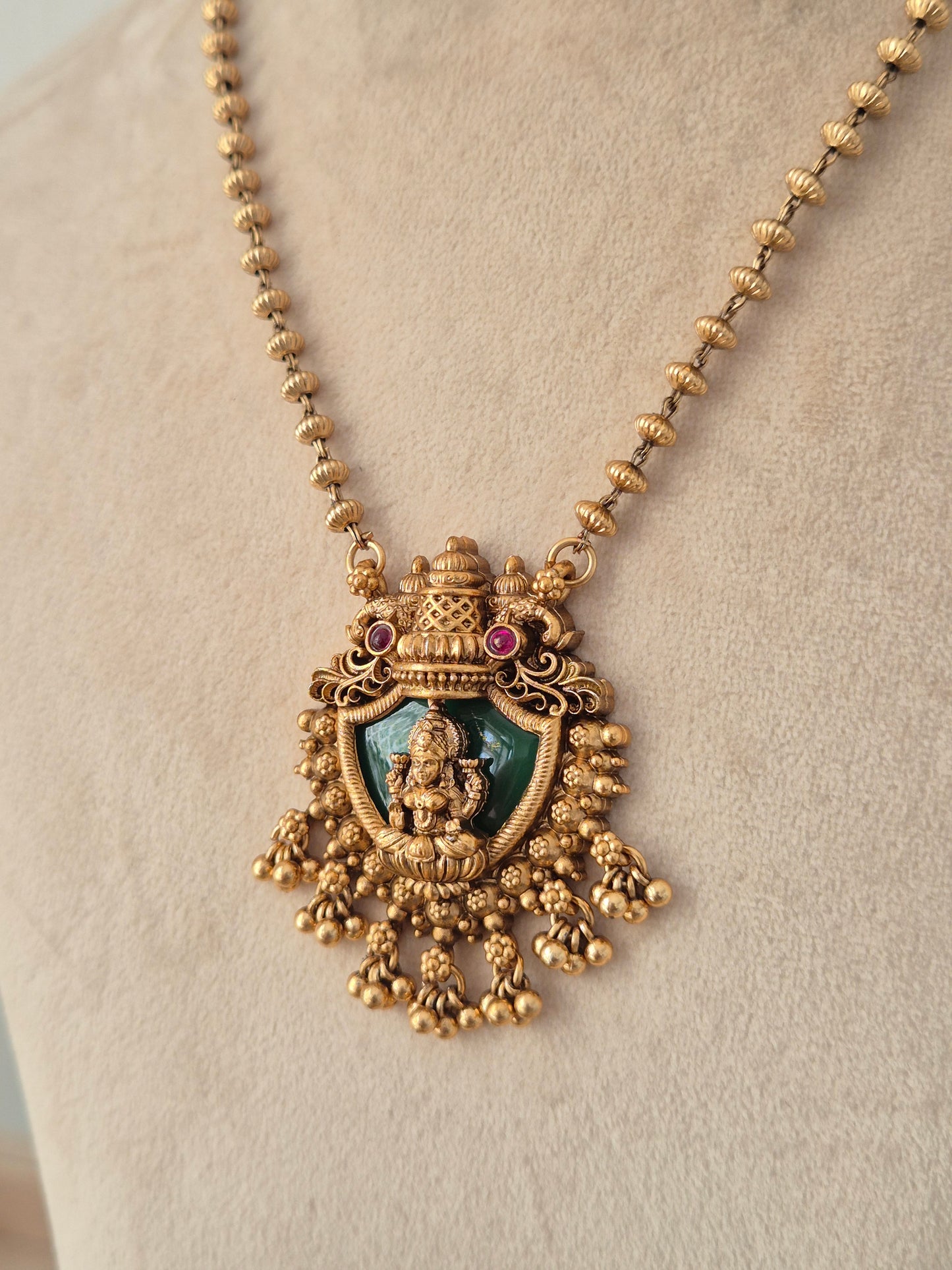 Charumati Necklace Set close-up view of antique gold temple pendant with green enamel Lakshmi motif by Naitri.