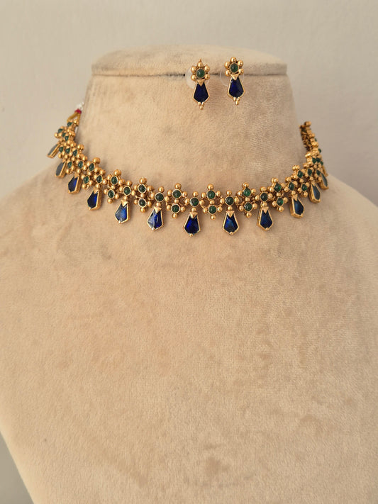 Ehsaas Necklace Set featuring a classic gold-toned choker encrusted with rectangular emerald-green stones and intricate Kundan-style borders, finished with dangling cream pearl clusters, displayed on a mannequin bust with matching drop earrings