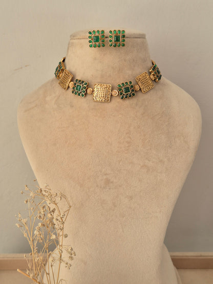 Lambika Necklace Set showcasing an antique gold-toned choker adorned with alternating square metal motifs and cluster-set green CZ stone accents, displayed on a beige mannequin bust with matching square studs