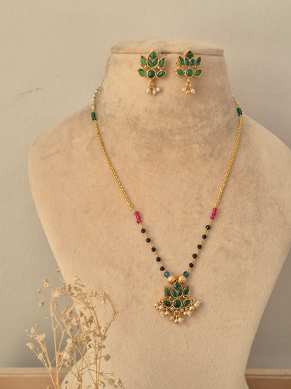 Prabhati Necklace Set showcasing a gold-toned chain with colorful bead stations and a green stone lotus-shaped pendant with pearl drops, displayed on a beige mannequin bust with matching floral stud earrings