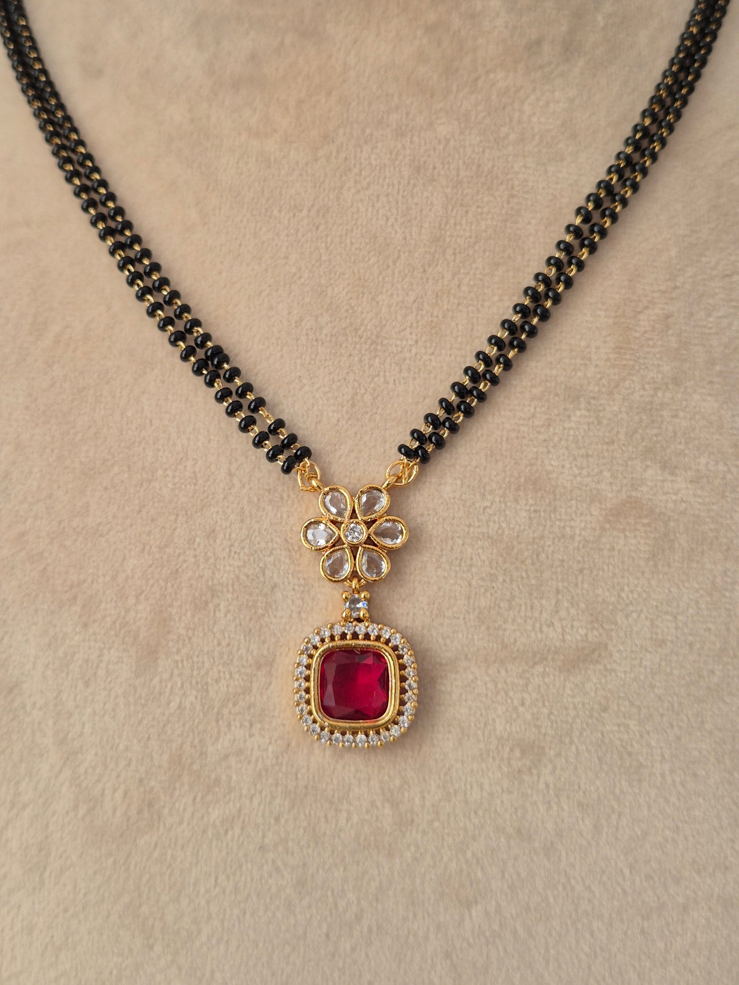 Prisham Mangalsutra close-up view of gold floral pendant with red CZ stone and black bead chain by Naitri