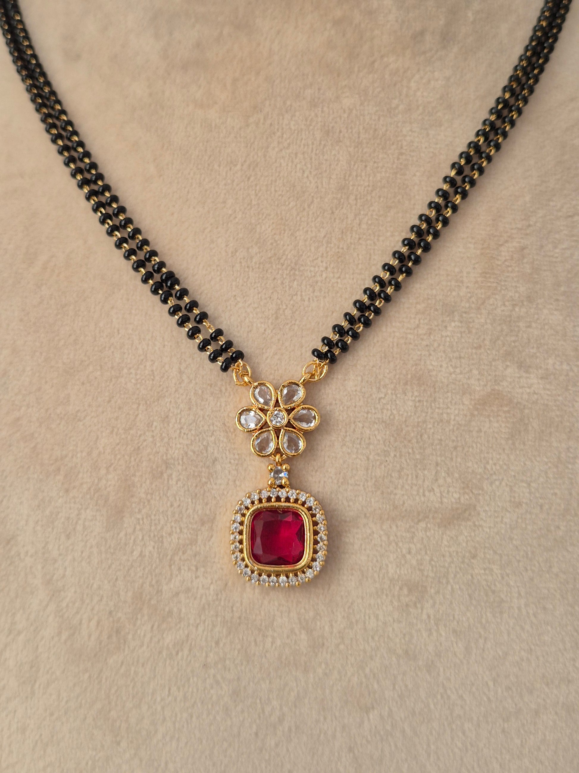Prisham Mangalsutra close-up view of gold floral pendant with red CZ stone and black bead chain by Naitri